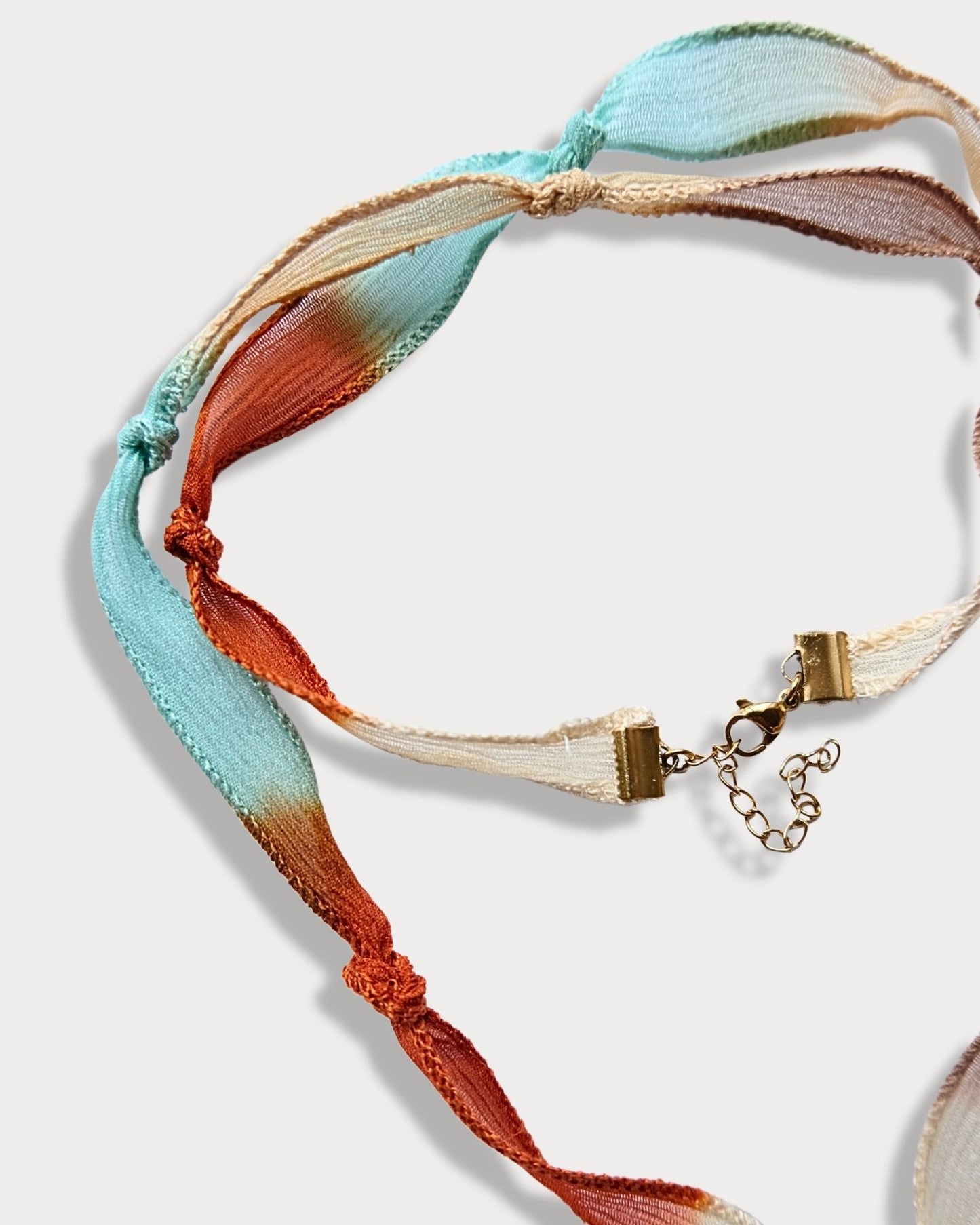 Collana in seta annodata azzurro, arancio e rosa con pendente a forma di cuore e pietra del sole