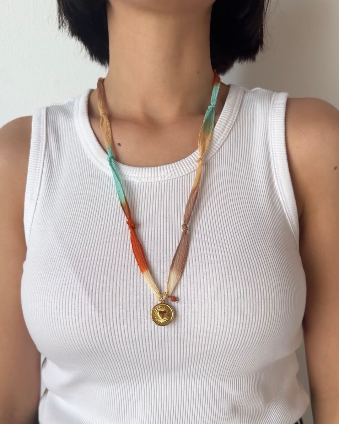 Collana in seta annodata azzurro, arancio e rosa con pendente a forma di cuore e pietra del sole